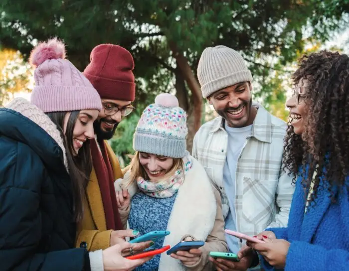 Group of multiracial young friends with coats and hats, smiling and watching the social media with a